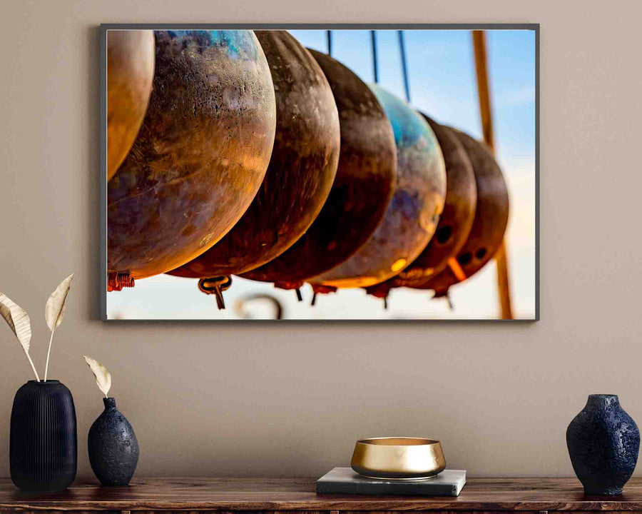 Wall art of Artist Andre Chambers, featuring an image of several rusted bouy's, in a line, suspended in air. The image is framed, on a wall, in a living room of a home.